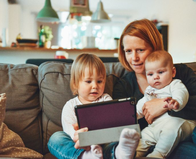 middle aged mother with two young children looking at a tablet on a couch