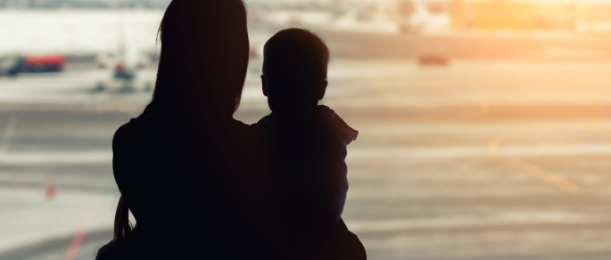 Silhouette of young woman experiencing family violence holding a young child against sunset background