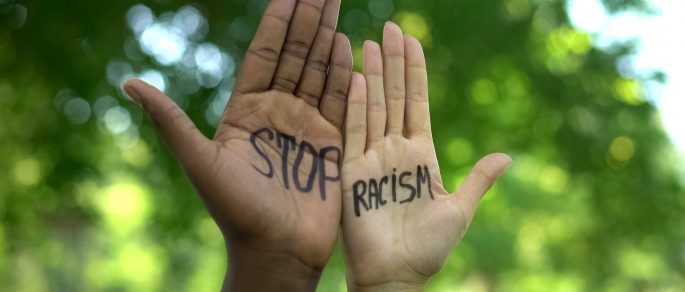 Two culturally diverse hands being held up next to each other with the words stop racism written on them