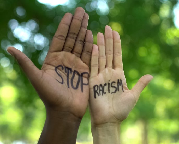 Two culturally diverse hands being held up next to each other with the words stop racism written on them