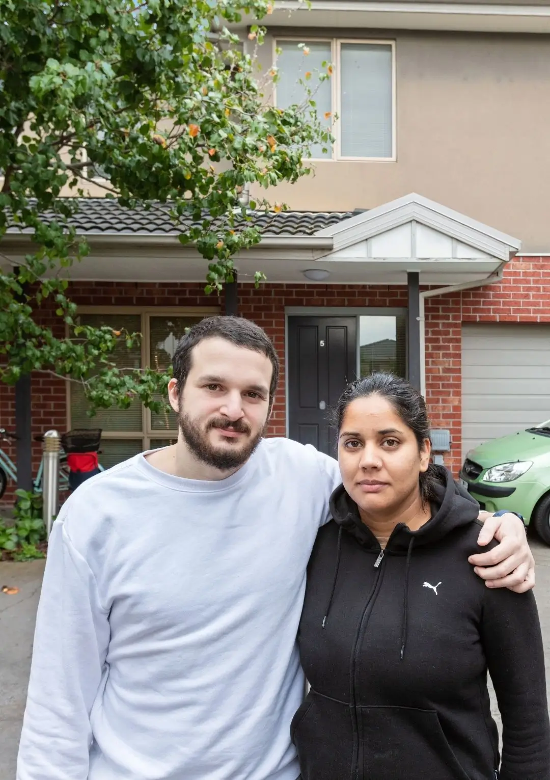 Closeup of serious looking couple in front of brick rented house