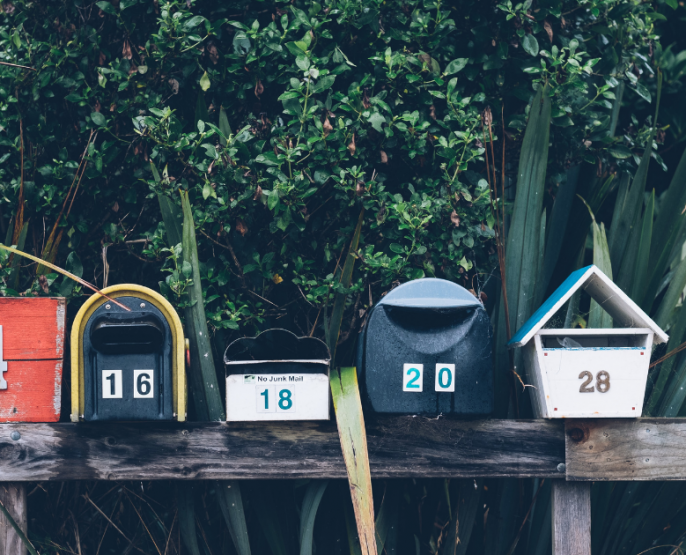 Group of six mailboxes in different shapes and colours against green foliage