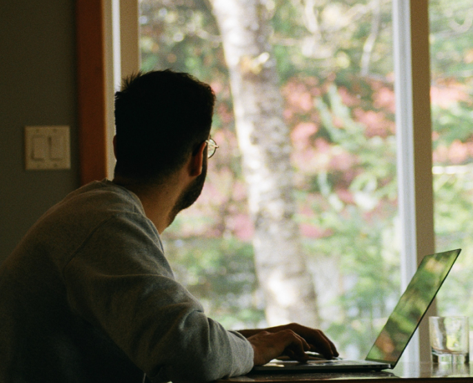Depressed man in glasses with laptop looking out window